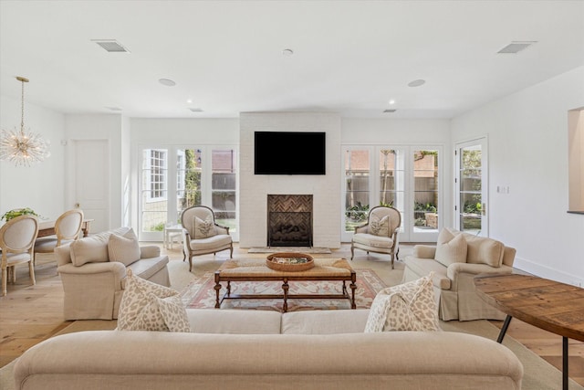 living room featuring an inviting chandelier, a brick fireplace, and light hardwood / wood-style flooring