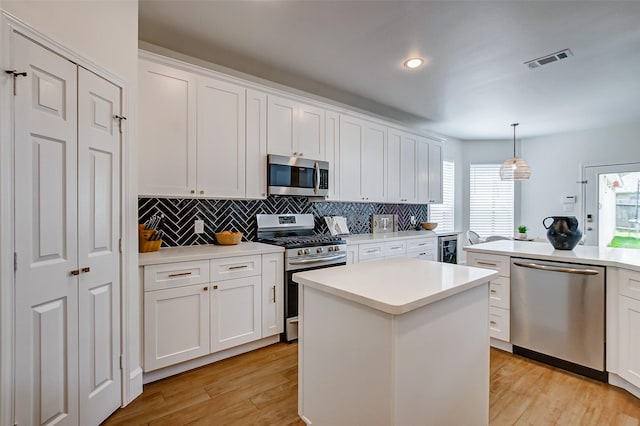 kitchen with decorative light fixtures, stainless steel appliances, white cabinets, and a kitchen island