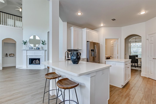 kitchen with white cabinetry, a center island, a fireplace, light hardwood / wood-style floors, and stainless steel fridge with ice dispenser