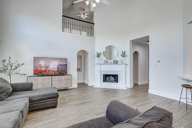 living room with a high ceiling, ceiling fan, light wood-type flooring, and a fireplace