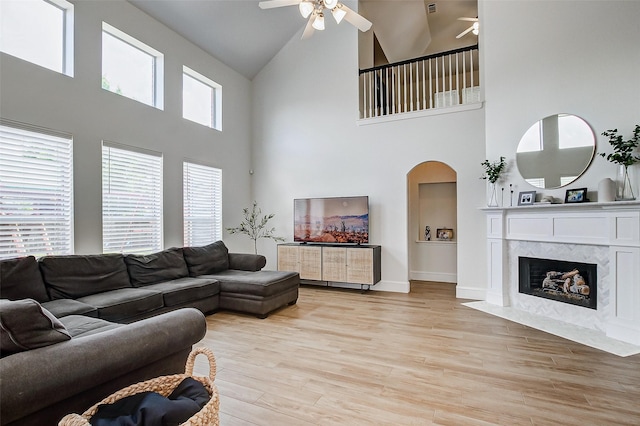 living room with a towering ceiling, a fireplace, light hardwood / wood-style floors, and ceiling fan