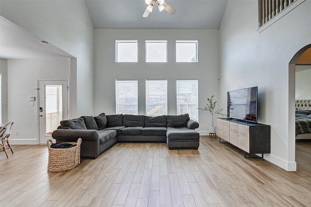 living room with a high ceiling, ceiling fan, and light hardwood / wood-style flooring