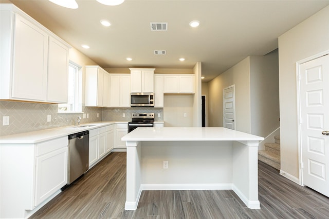 kitchen with a center island, appliances with stainless steel finishes, white cabinets, hardwood / wood-style floors, and backsplash