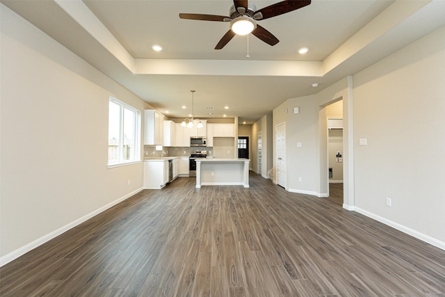 unfurnished living room with ceiling fan with notable chandelier, dark hardwood / wood-style flooring, and a tray ceiling