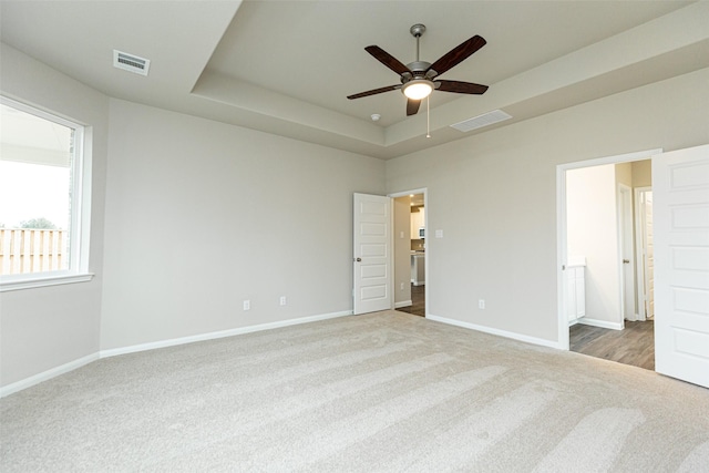 unfurnished bedroom featuring ceiling fan, light colored carpet, a tray ceiling, and ensuite bath