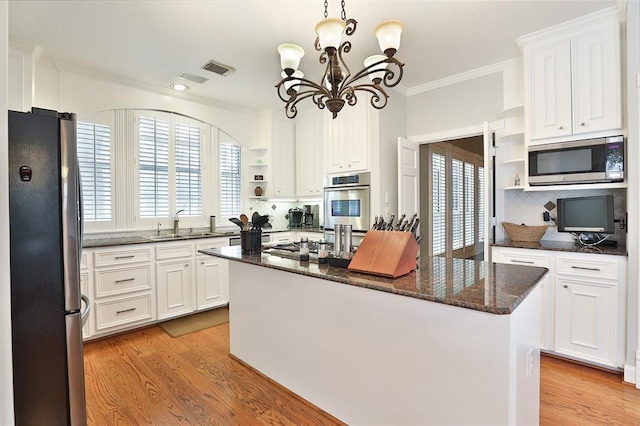 kitchen with pendant lighting, dark stone countertops, stainless steel appliances, white cabinets, and a kitchen island