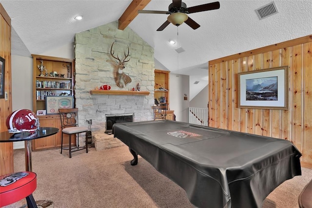 recreation room with carpet floors, lofted ceiling with beams, a textured ceiling, a stone fireplace, and wood walls