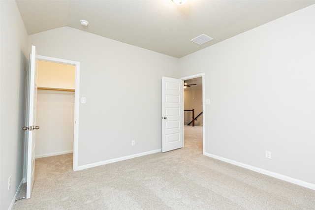 unfurnished bedroom with vaulted ceiling, a walk in closet, light colored carpet, and a closet