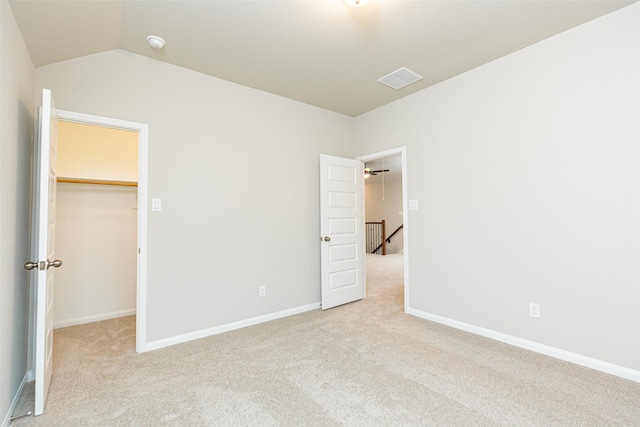 unfurnished bedroom with light colored carpet, a spacious closet, vaulted ceiling, and a closet