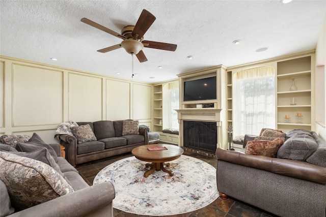 living room with ceiling fan, built in shelves, and a textured ceiling