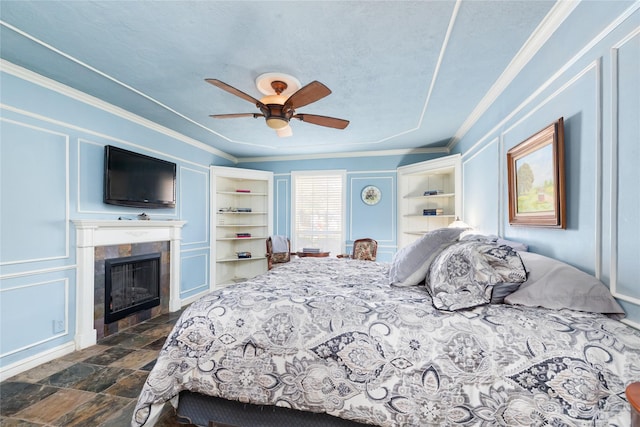 bedroom with a tile fireplace, crown molding, a textured ceiling, and ceiling fan