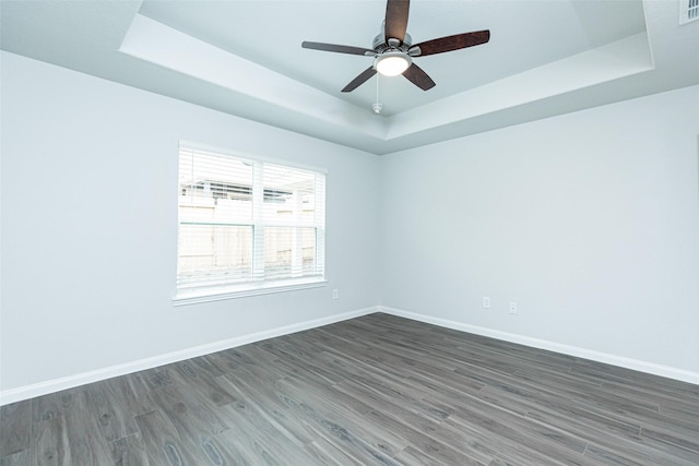 unfurnished room featuring a raised ceiling, ceiling fan, and dark hardwood / wood-style flooring