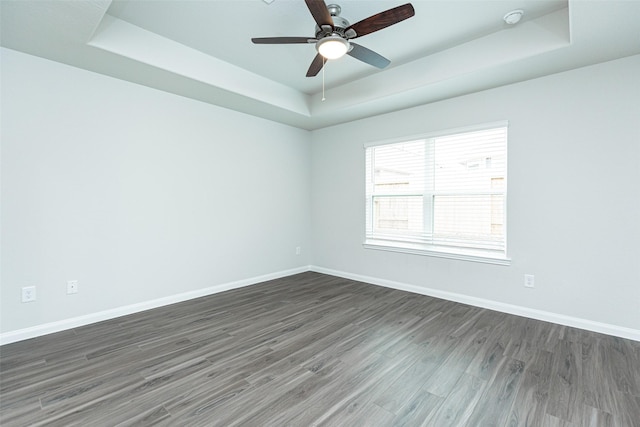 empty room with a tray ceiling, dark hardwood / wood-style floors, and ceiling fan