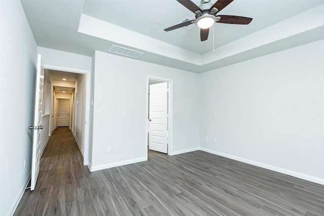 unfurnished bedroom with a raised ceiling, dark hardwood / wood-style floors, and ceiling fan