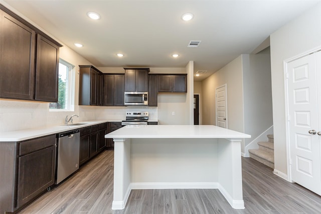 kitchen featuring dark brown cabinets, light wood-type flooring, appliances with stainless steel finishes, a kitchen island, and backsplash