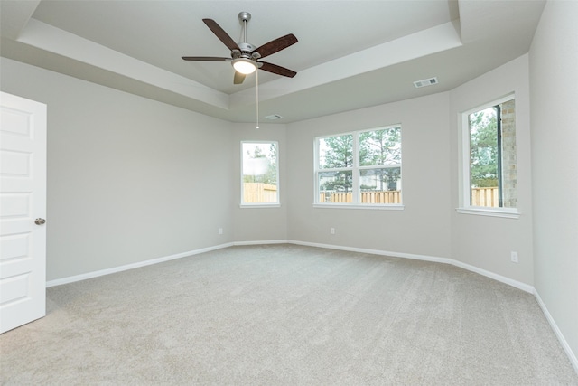 spare room featuring a raised ceiling, light colored carpet, and ceiling fan