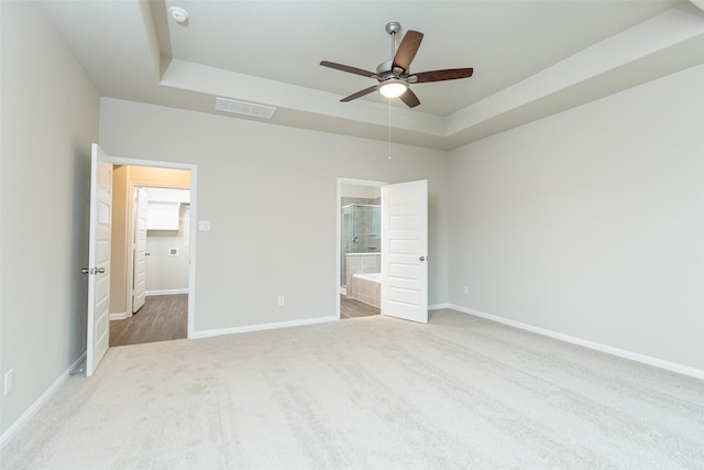 unfurnished bedroom with ceiling fan, ensuite bath, a raised ceiling, and carpet