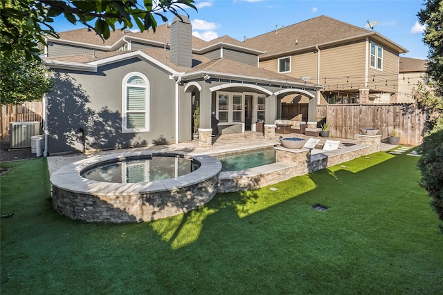 rear view of house with an in ground hot tub, a lawn, and a patio area