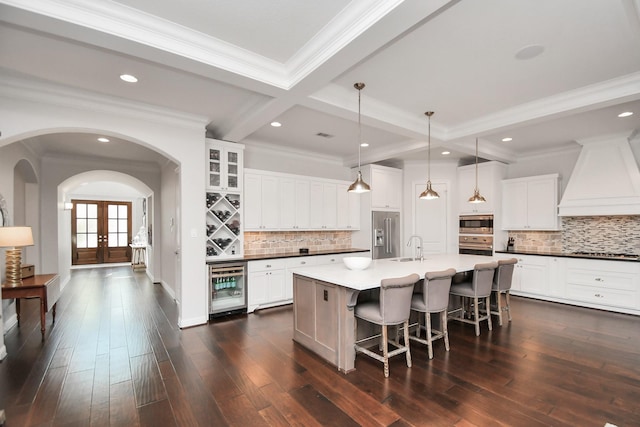 kitchen with wine cooler, appliances with stainless steel finishes, custom range hood, and white cabinets