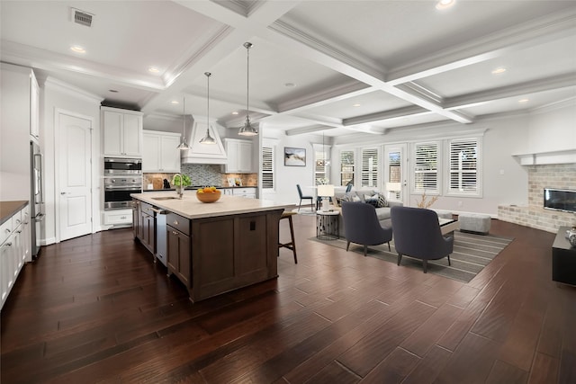 kitchen with pendant lighting, sink, white cabinetry, stainless steel appliances, and a center island with sink