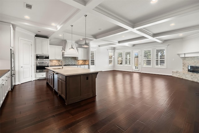 kitchen with pendant lighting, sink, white cabinets, stainless steel appliances, and a center island with sink