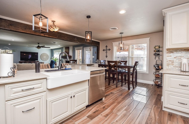 kitchen with decorative light fixtures, sink, white cabinets, stainless steel dishwasher, and light wood-type flooring