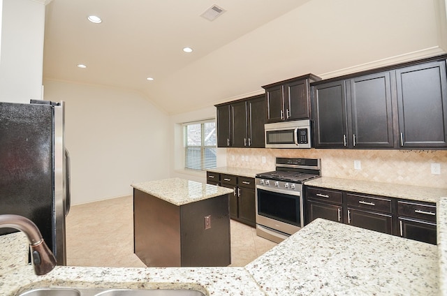 kitchen featuring lofted ceiling, backsplash, stainless steel appliances, light stone countertops, and light tile patterned flooring