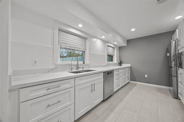 kitchen with appliances with stainless steel finishes, white cabinetry, sink, decorative backsplash, and light stone countertops