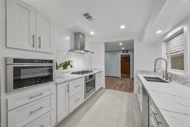 kitchen with sink, range hood, white cabinets, and appliances with stainless steel finishes