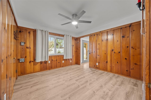 empty room featuring light hardwood / wood-style flooring, ceiling fan, and wood walls