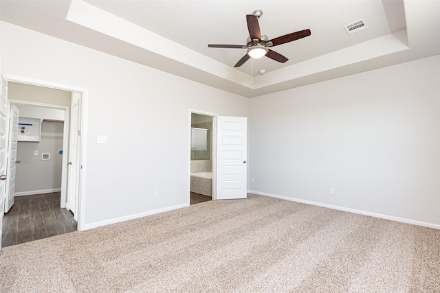 unfurnished bedroom with ceiling fan, ensuite bath, a tray ceiling, and a spacious closet