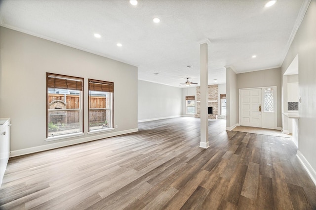 unfurnished living room with hardwood / wood-style flooring, ornamental molding, a stone fireplace, and ceiling fan