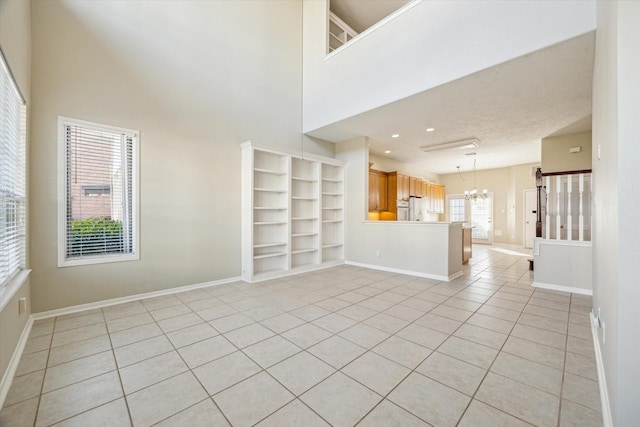 unfurnished living room featuring a notable chandelier, a towering ceiling, built in features, and light tile patterned flooring