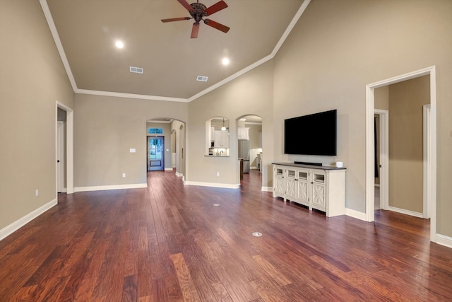 unfurnished living room featuring a towering ceiling, dark wood-type flooring, ornamental molding, and ceiling fan