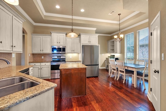 kitchen featuring decorative light fixtures, sink, a tray ceiling, stainless steel appliances, and light stone countertops