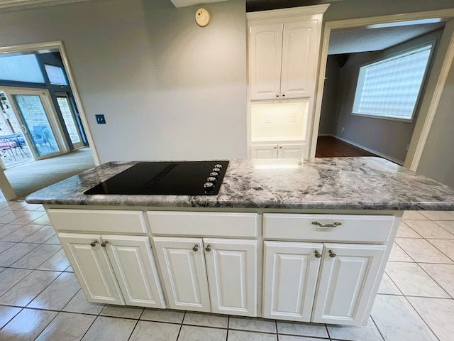 kitchen featuring light tile patterned floors, black electric stovetop, dark stone counters, and white cabinets