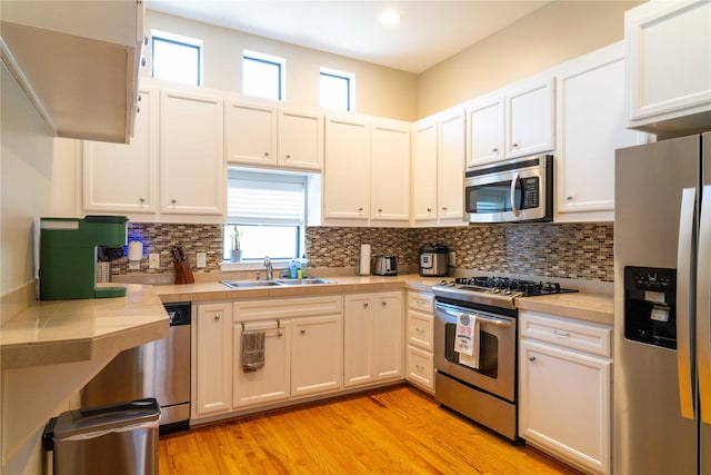 kitchen with sink, light wood-type flooring, appliances with stainless steel finishes, decorative backsplash, and white cabinets