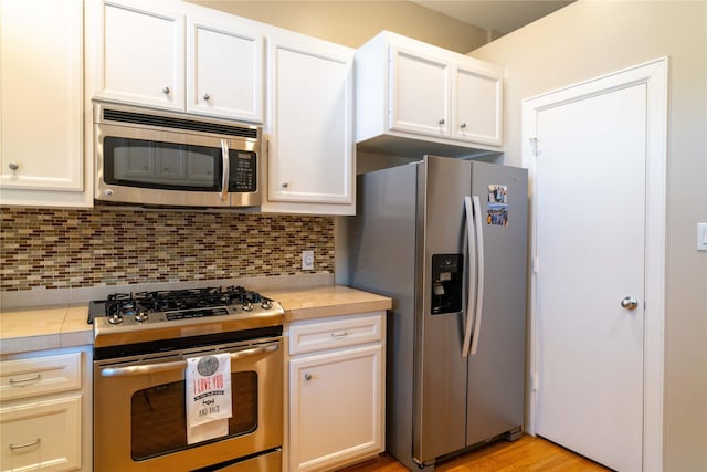 kitchen with stainless steel appliances, tasteful backsplash, light wood-type flooring, and white cabinetry