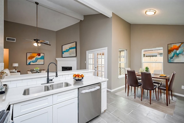 kitchen featuring sink, beam ceiling, stainless steel dishwasher, a fireplace, and white cabinets