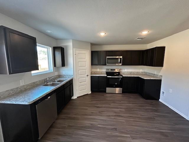 kitchen featuring stainless steel appliances, light countertops, visible vents, dark wood-type flooring, and a sink