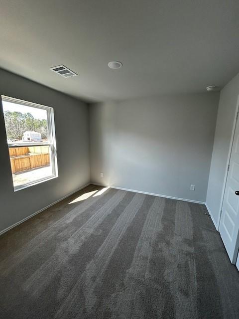 spare room with visible vents, dark carpet, and baseboards