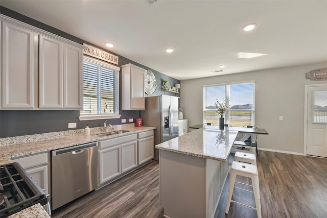 kitchen with a kitchen island, appliances with stainless steel finishes, sink, dark hardwood / wood-style flooring, and light stone countertops