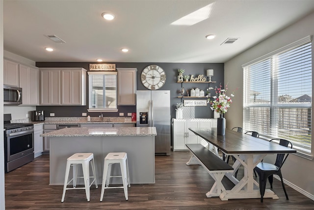 kitchen with a kitchen island, appliances with stainless steel finishes, a breakfast bar, dark hardwood / wood-style flooring, and light stone counters