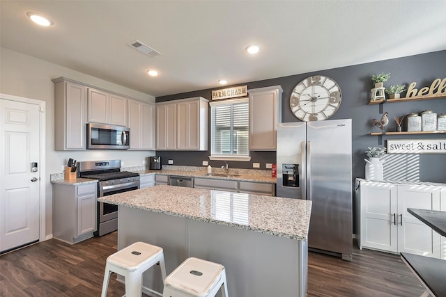 kitchen featuring a kitchen island, appliances with stainless steel finishes, dark hardwood / wood-style floors, a kitchen bar, and light stone counters