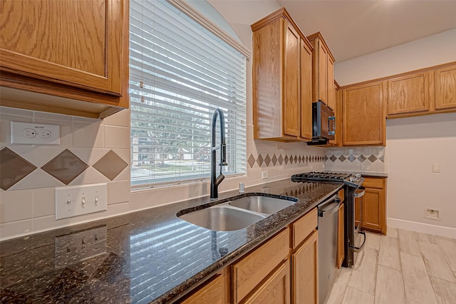 kitchen featuring sink, light wood-type flooring, dark stone countertops, stainless steel appliances, and decorative backsplash