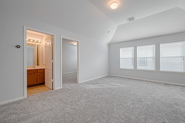 unfurnished bedroom with a walk in closet, ensuite bathroom, vaulted ceiling, and light carpet