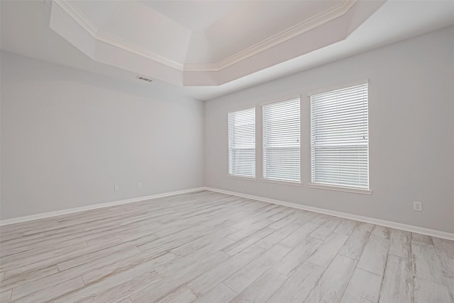 empty room with ornamental molding, a raised ceiling, and light hardwood / wood-style floors