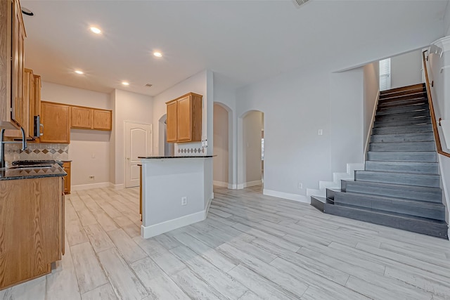 kitchen with light hardwood / wood-style floors, sink, decorative backsplash, and dark stone countertops