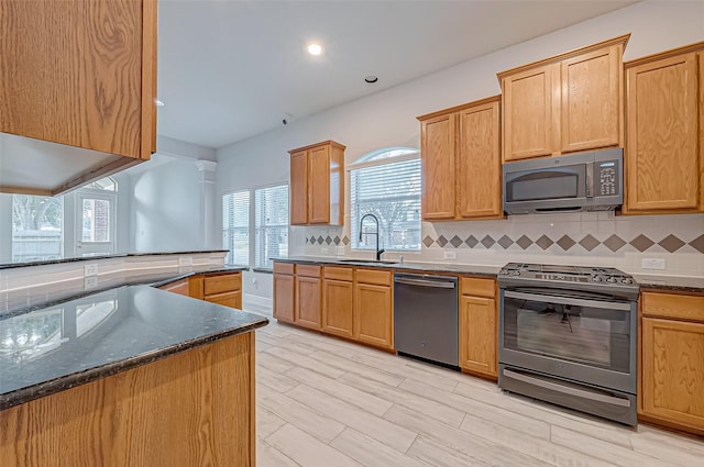 kitchen with sink, decorative backsplash, stainless steel appliances, and dark stone counters