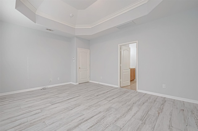 empty room featuring a raised ceiling, crown molding, and light wood-type flooring